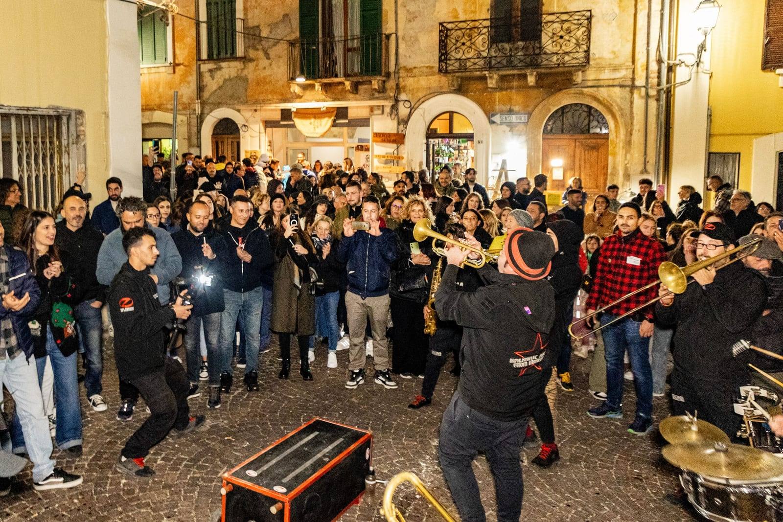 Una banda di fiati suona tra la folla in una piazzetta illuminata