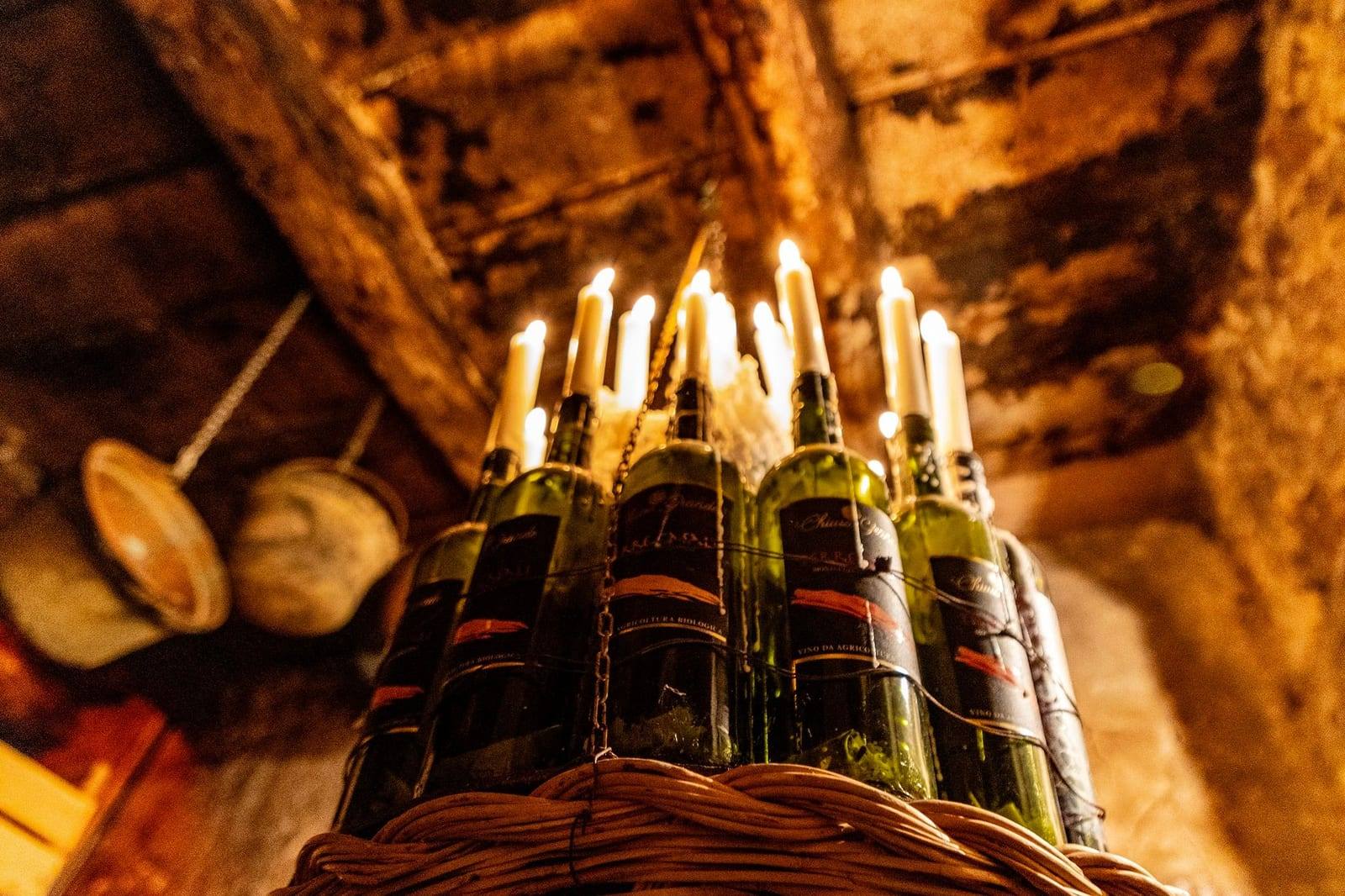 Bottiglie di vino con le candele accese in un cesto, nella luce calda di una cantina