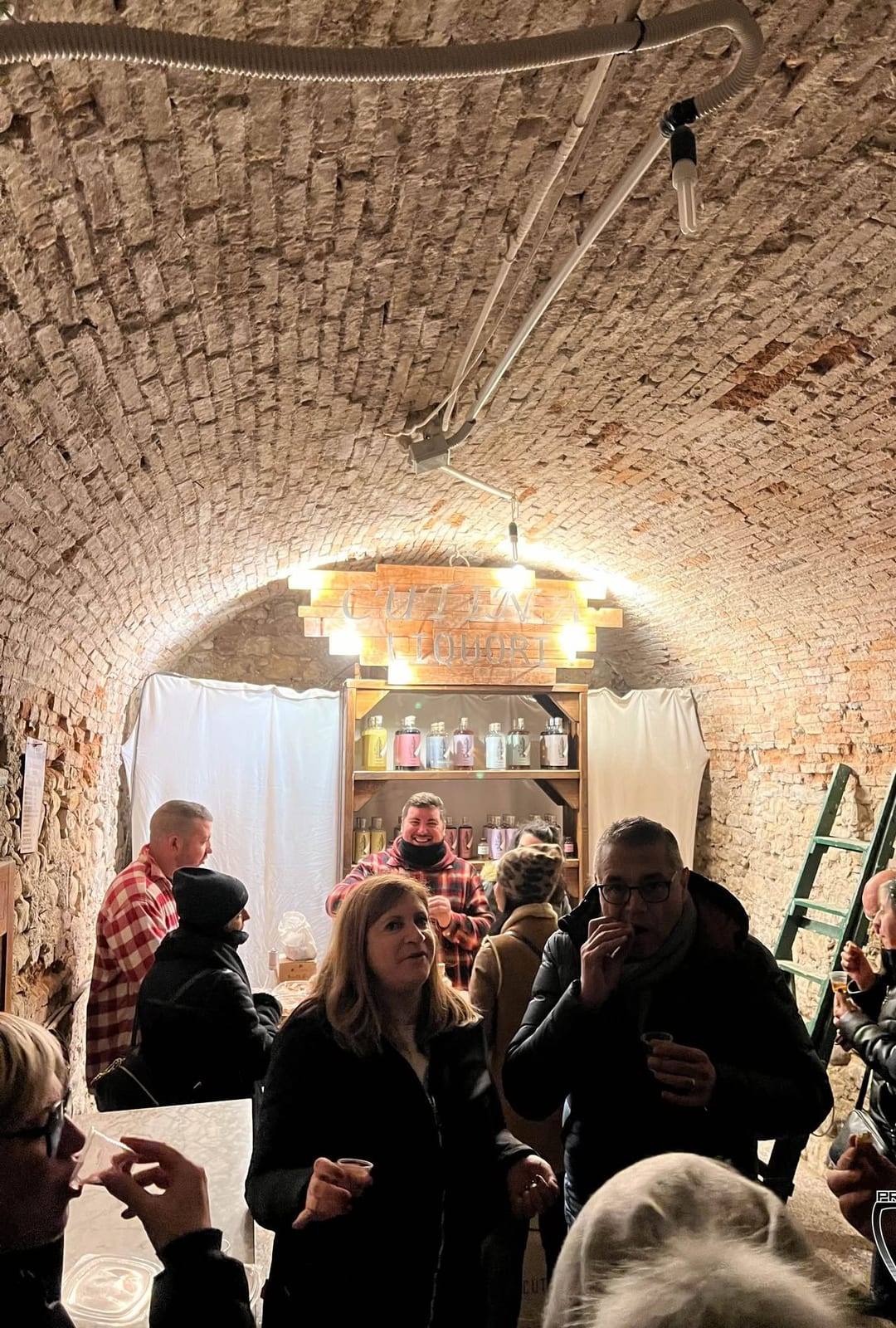 Interno di una cantina con volta in mattoni e visitatori con i calici