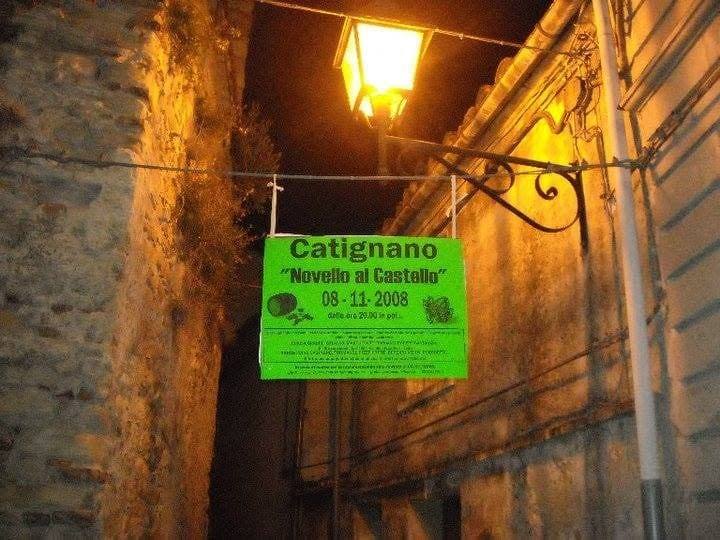 Cartello verde appeso in un vicolo di pietra sotto un lampione, con la scritta “Catignano – Novello al Castello, 08-11-2008”