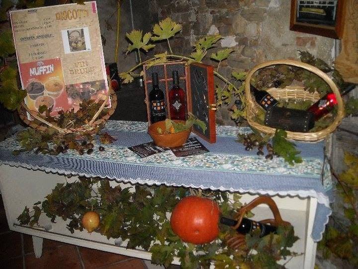 Un tavolo con tovaglia azzurra decorato con foglie di vite, un cesto, bottiglie di vino in una cassetta e una zucca