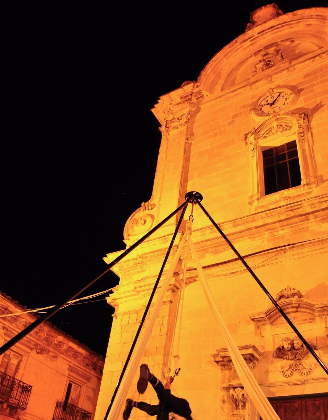 Un’acrobata aerea appesa ai tessuti davanti alla facciata illuminata della chiesa