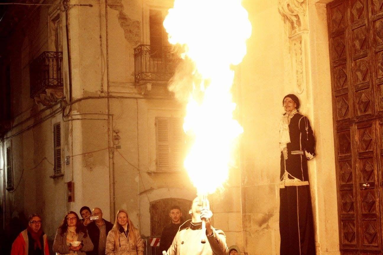 Un mangiafuoco sputa una fiammata accanto a un trampoliere in un vicolo del borgo