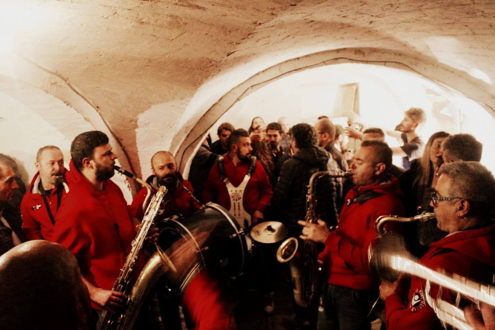 Una banda in felpe rosse suona tra la folla sotto una volta in pietra