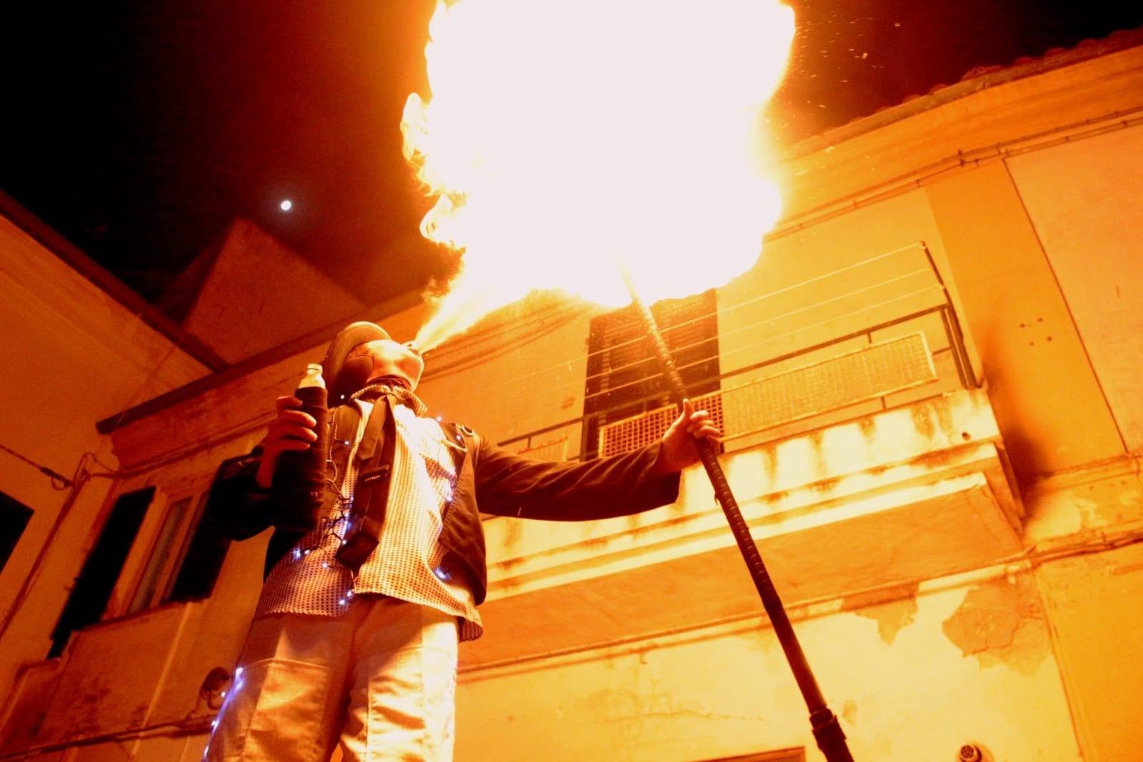 Un mangiafuoco sputa una fiammata tra le case del borgo di notte