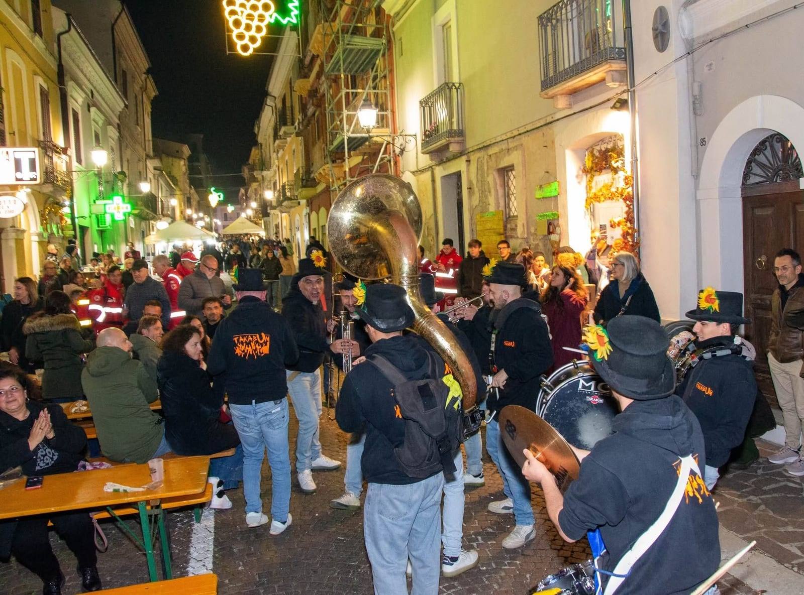 Banda di fiati con la tuba nel corso illuminato dalle luminarie a grappolo